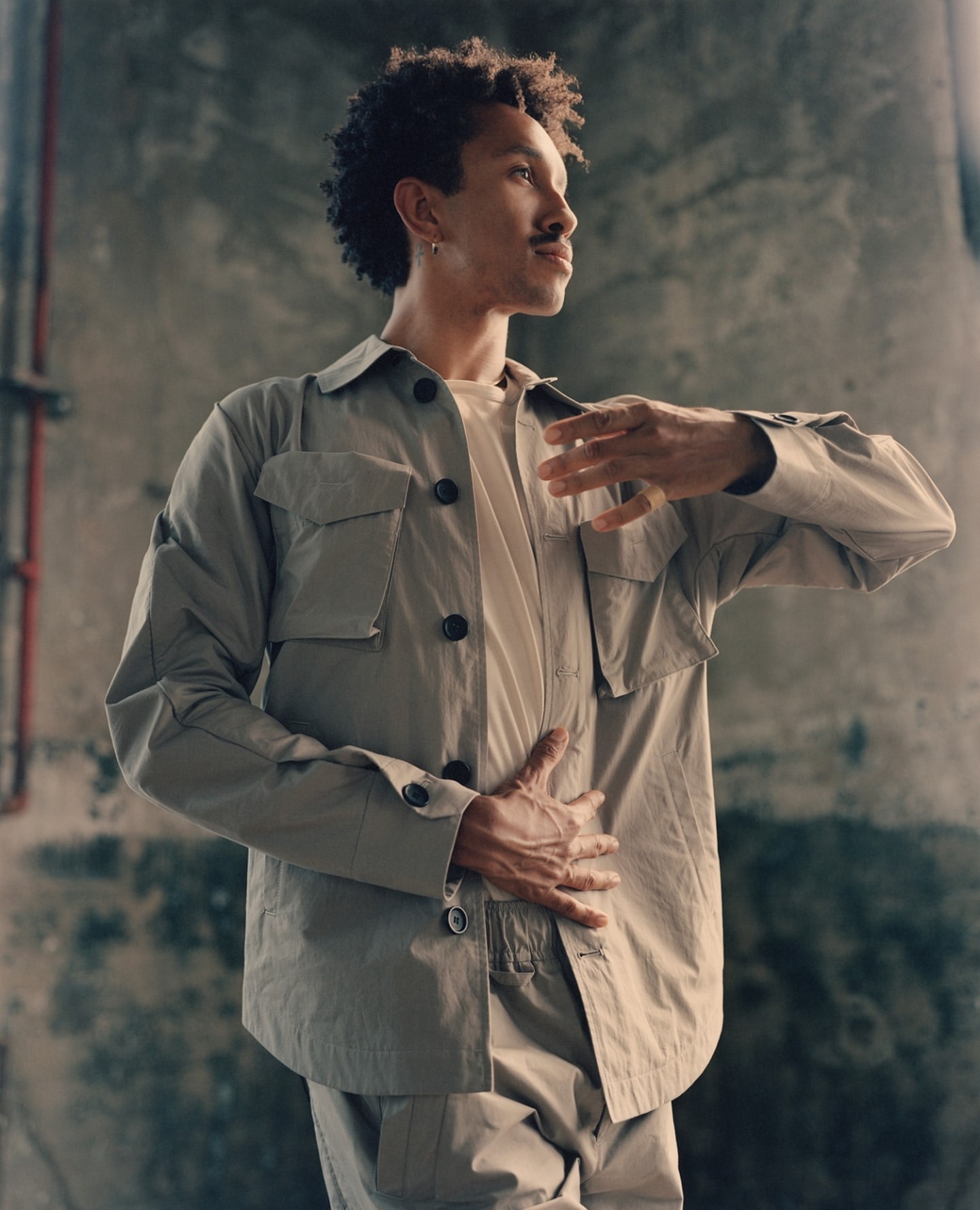 Studio shot of a curly-haired man in a beige collared jacket with an abstract background. Fashion editorial with natural light.