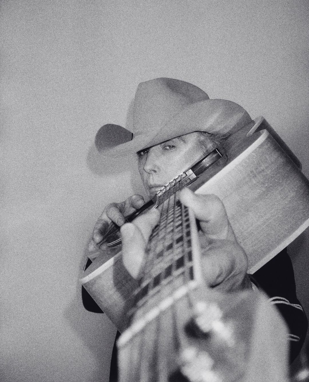 Monochrome portrait of adult with cowboy hat playing guitar, close-up, indoors.