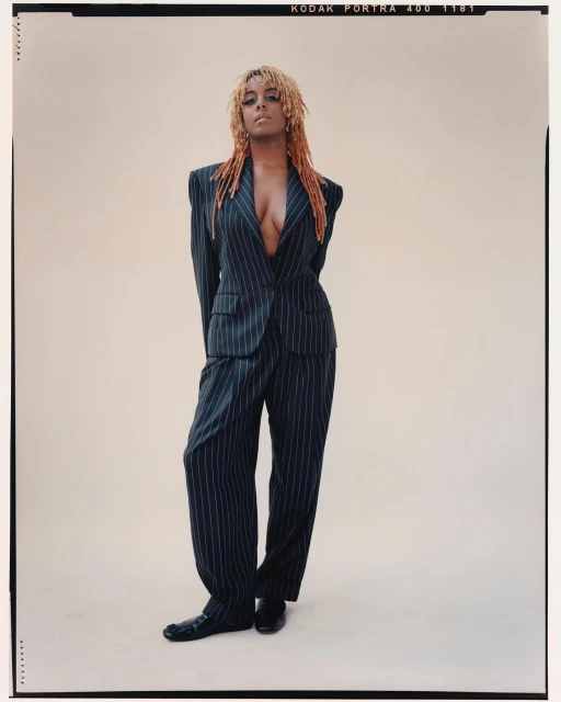 Adult female fashion model in pinstripe suit posing in studio with arms behind her back, looking at the camera. Cool studio lighting.