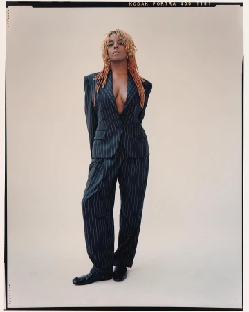 Adult female fashion model in pinstripe suit posing in studio with arms behind her back, looking at the camera. Cool studio lighting.