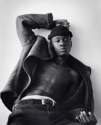 Black man wearing a beanie and an open shearling jacket against a white background by photographer Andreas Laszlo Konrath.