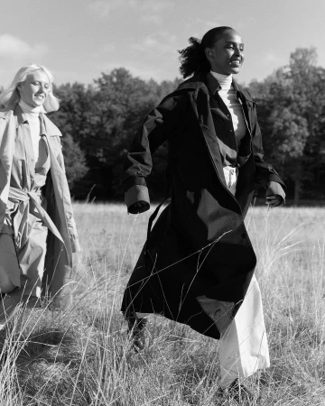 Black and white portrait of two women walking through a grassy field wearing long coats and turtlenecks by Andreas Ohlund.