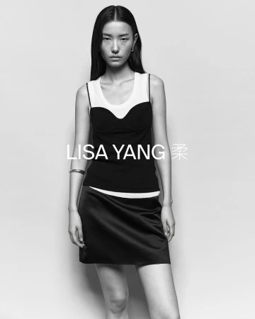 Black and white portrait of a young woman wearing a black and white top and a short black skirt against a plain backdrop.