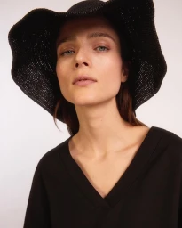 Portrait of a woman wearing a wide brim black woven sun hat and a black v-neck top against a plain white background