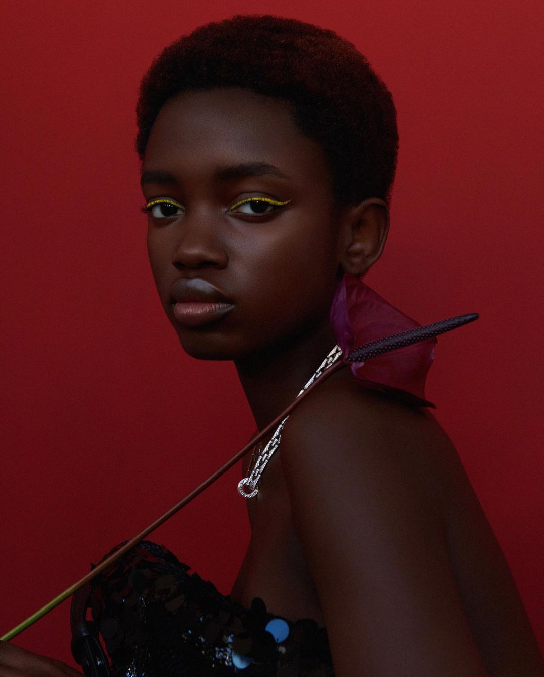 Close-up portrait of a young Black woman with an anthurium flower, red backdrop, minimal makeup and an elegant, stylish aesthetic.