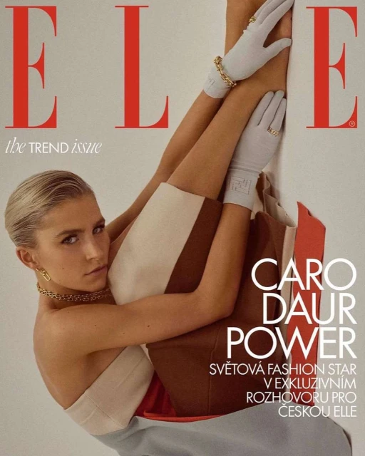 Fashion editorial cover of Elle magazine featuring a blonde female model in light-colored modern clothing, gold jewelry, and white gloves.