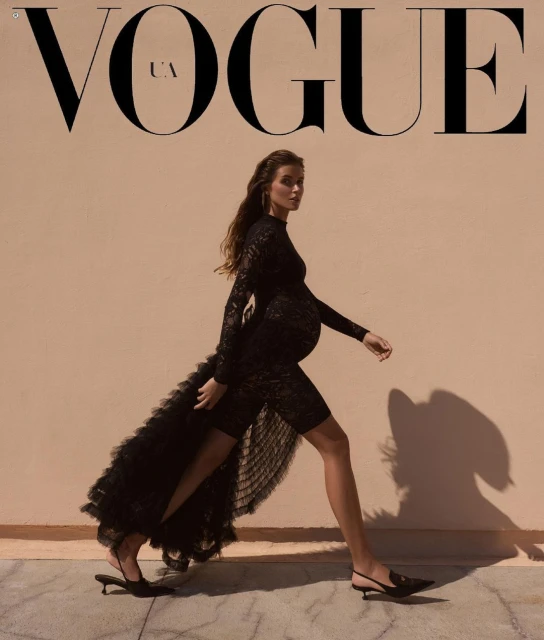 Vogue UA cover features a pregnant model in a black lace dress walking against a neutral background, showcasing fashion and elegance.