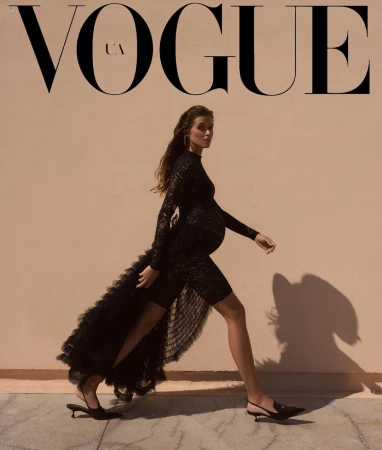 Vogue UA cover features a pregnant model in a black lace dress walking against a neutral background, showcasing fashion and elegance.