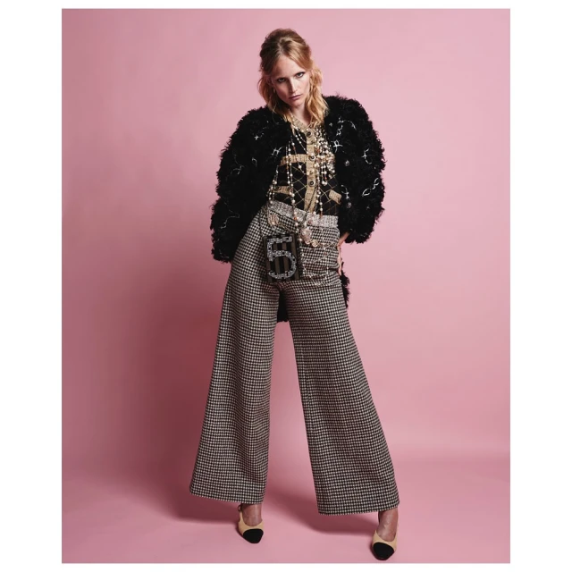 Full-length shot of a female fashion model wearing a black and gold jacket, patterned wide-leg pants, jewelry, and black and beige heels.