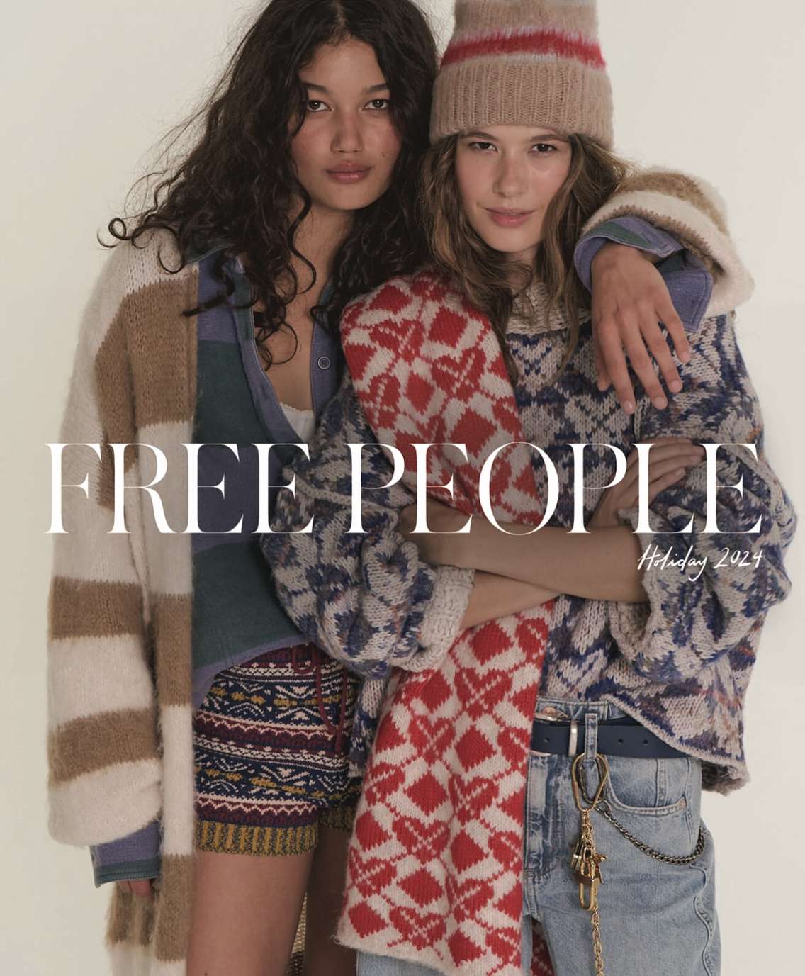 Two women pose in knit sweaters and shorts for Free People's Holiday 2024 collection, showcasing winter fashion against a neutral backdrop.