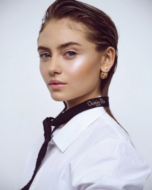 Close-up studio shot of a young adult female with wet hair, wearing a white shirt and a black ribbon around her neck, against a white background.