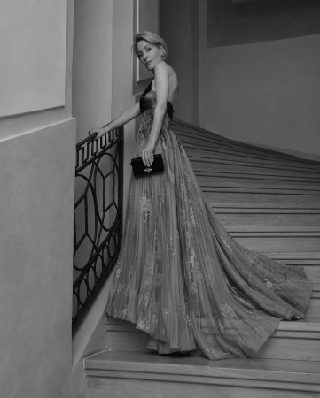 Gillian Anderson wearing a flowing evening gown on a grand staircase, holding a small clutch by Andreas Ortner