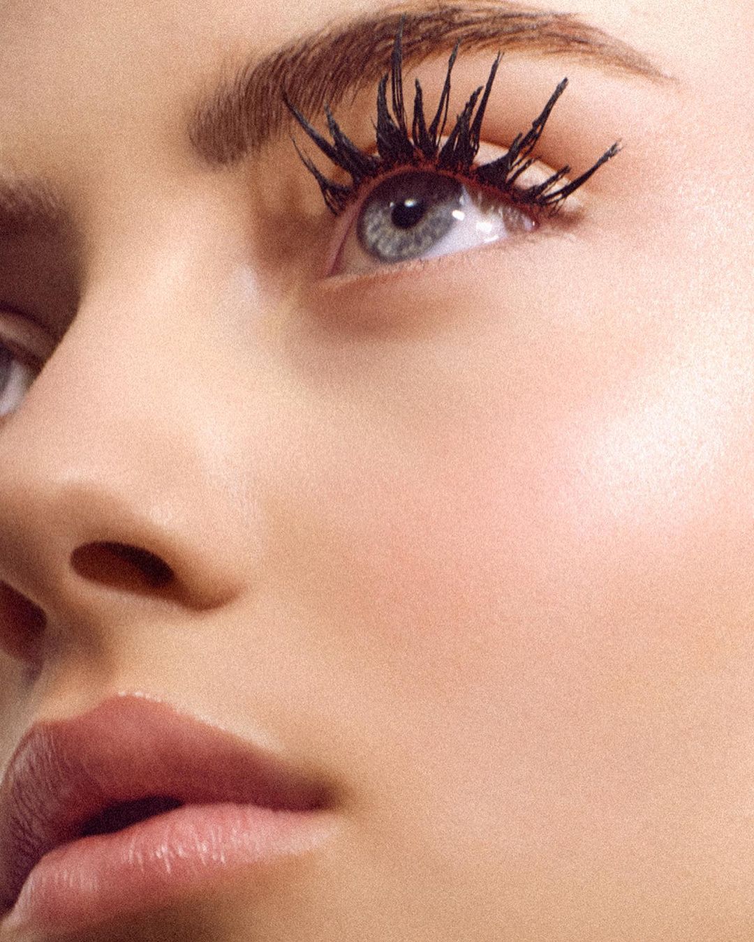 Close-up beauty portrait focusing on a woman's eye with heavily spiked black mascara and natural pink lips.