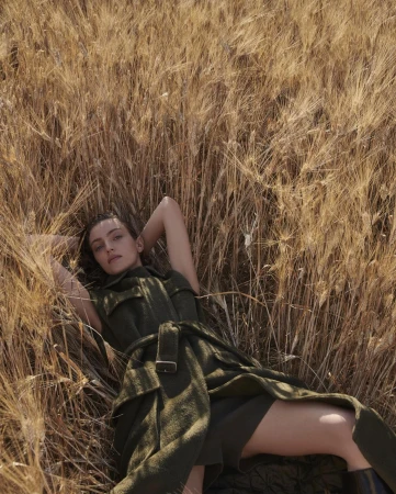 Woman in green dress lying in golden wheat field, looking at the camera. Outdoor fashion portrait in a rural landscape setting.