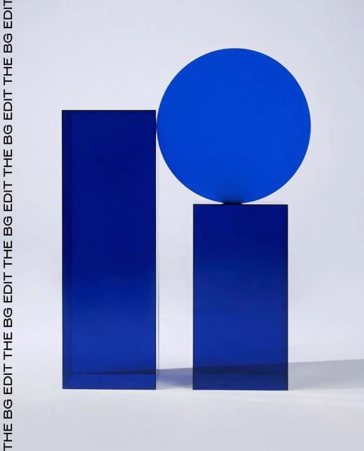 Abstract still life featuring a blue sphere resting atop a shorter blue rectangular block next to a taller blue rectangular block on white.