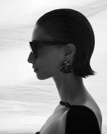Profile portrait of a woman wearing dark sunglasses and hoop earrings against a white background