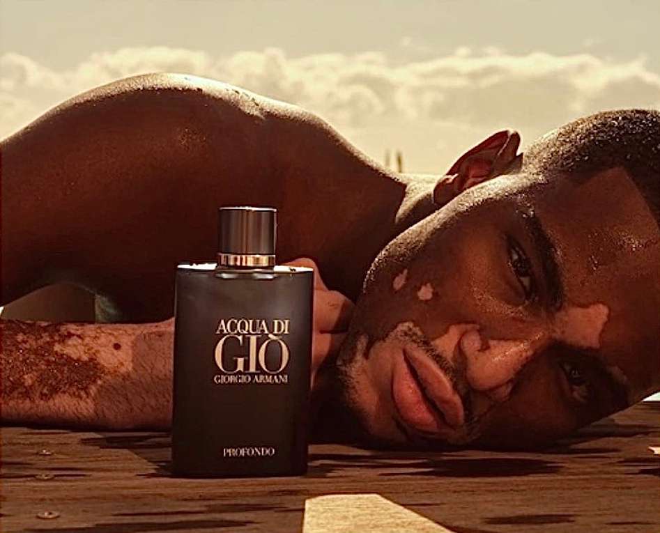 Close-up shot of Armani Acqua di Gio fragrance bottle with dark-skinned man lying on a wooden surface under a bright sky.
