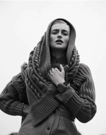Monochrome portrait of a woman with a neutral expression wearing a knitted hood and a leather-like coat against a light background.