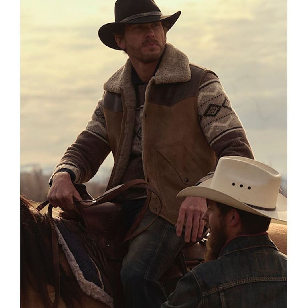 Two men on horseback, one wearing a black cowboy hat and a sheepskin vest, the other a white cowboy hat, in an outdoor setting.