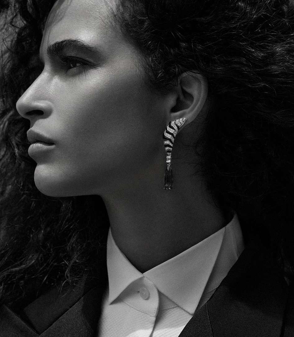 Elegant close-up of a woman's face in profile wearing a white collared shirt, black blazer, and a black and white dangling earring.