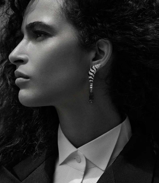 Elegant close-up of a woman's face in profile wearing a white collared shirt, black blazer, and a black and white dangling earring.