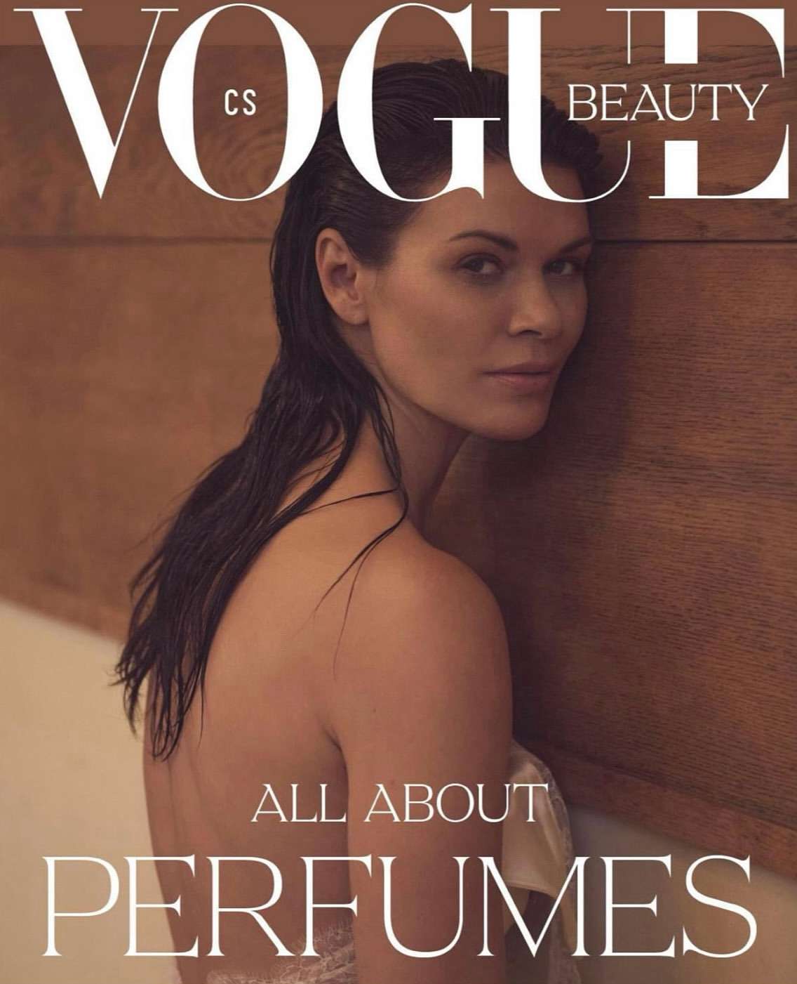 A woman with dark wet-look hair leaning against a wood panel wall in a beauty magazine cover portrait photograph by Andreas Ortner