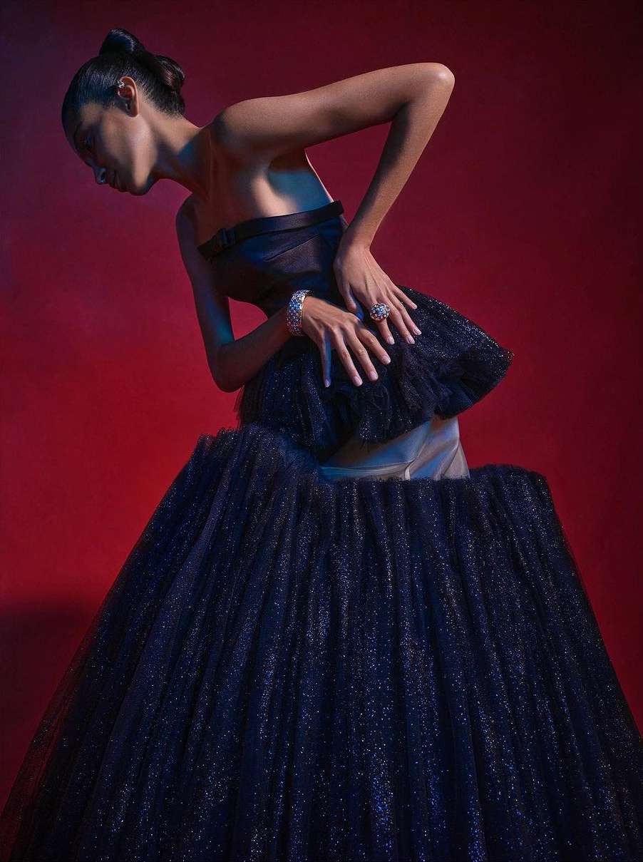 Model wearing a dark strapless structured gown posing dramatically against a deep red background