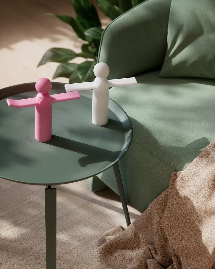 Indoor shot of two small figure sculptures in pink and white on a green table, with a green armchair and leafy plant in the background.