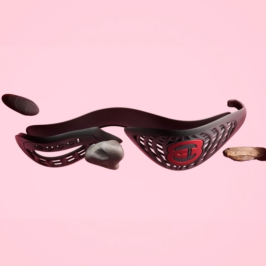 Black plastic headgear with red logo surrounded by floating rocks and wood on a pink background. Product shot for head protection.
