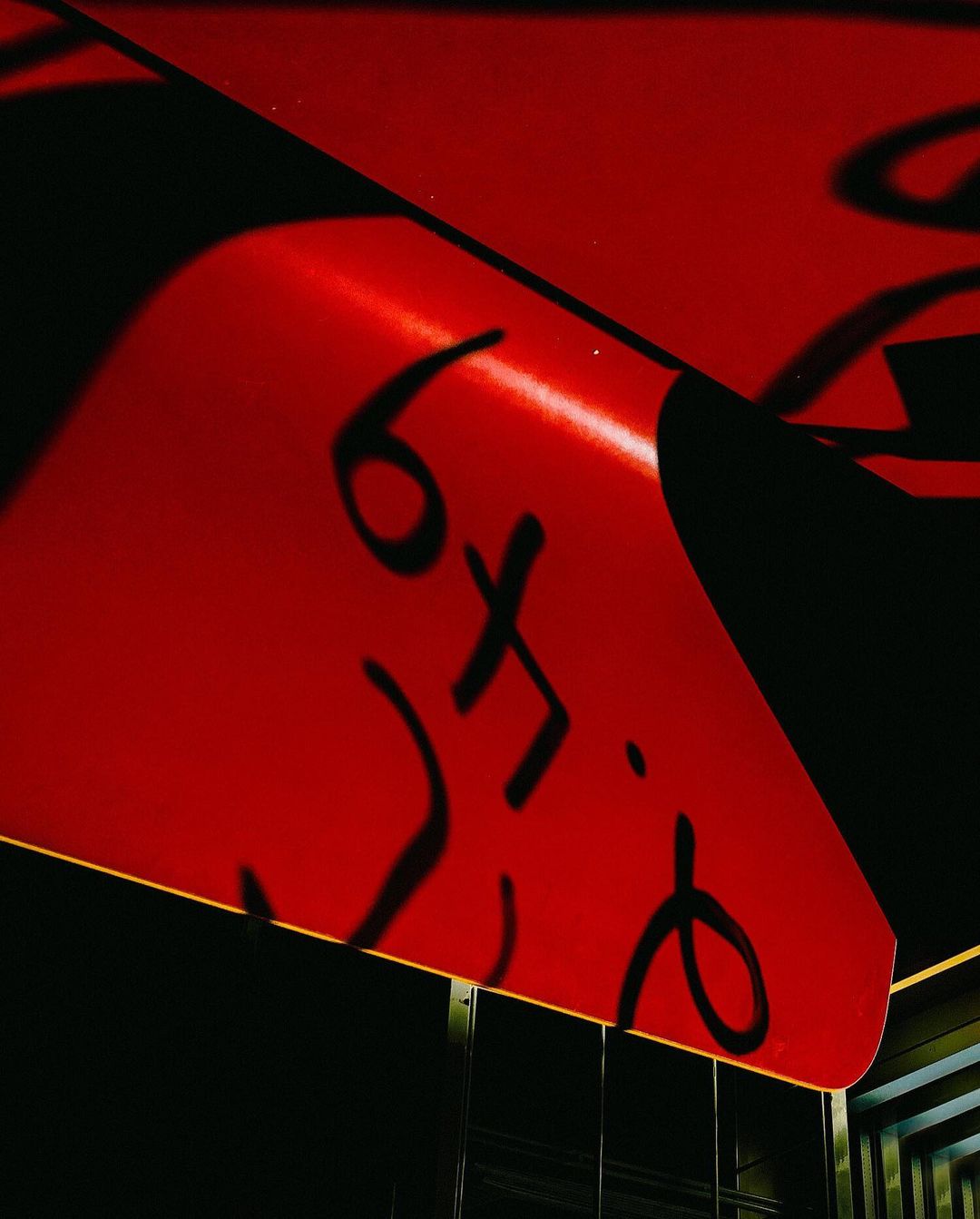 Abstract, low-angle shot of a red and black awning with stylized text casting a shadow, creating a graphic and modern composition.
