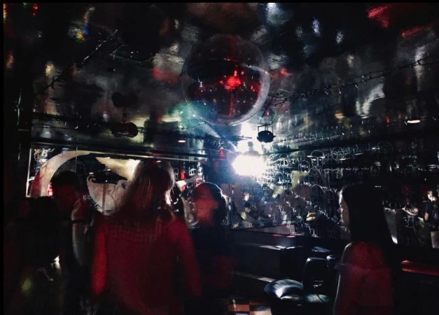 Crowd of people gathered inside a dark music venue with a disco ball, stage lights, and interior design details visible.