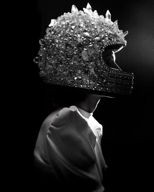 Profile shot of a person wearing a full-face motorcycle helmet entirely covered in crystals, against a dark background, in black and white.