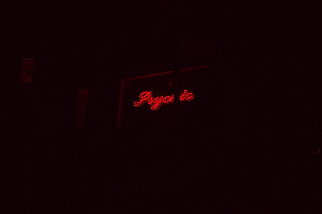 A neon sign glows red in the dark, displaying the word 'Psychic' in a cursive, retro style, creating a mysterious atmosphere.