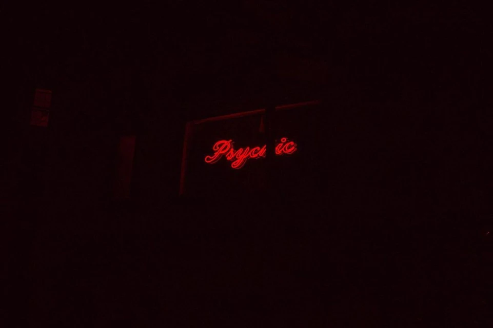 A neon sign glows red in the dark, displaying the word 'Psychic' in a cursive, retro style, creating a mysterious atmosphere.