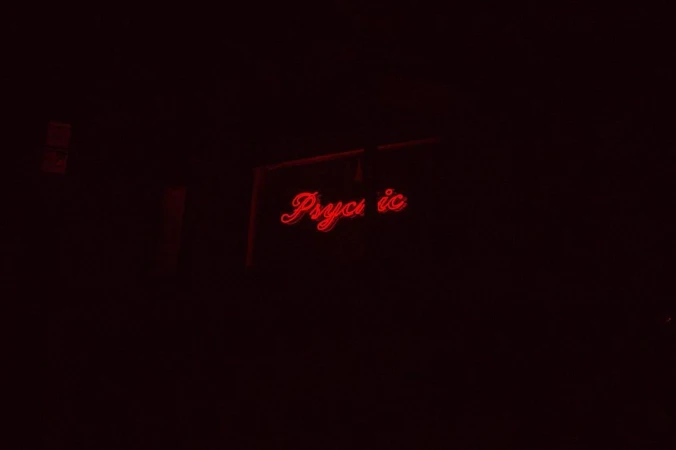 A neon sign glows red in the dark, displaying the word 'Psychic' in a cursive, retro style, creating a mysterious atmosphere.