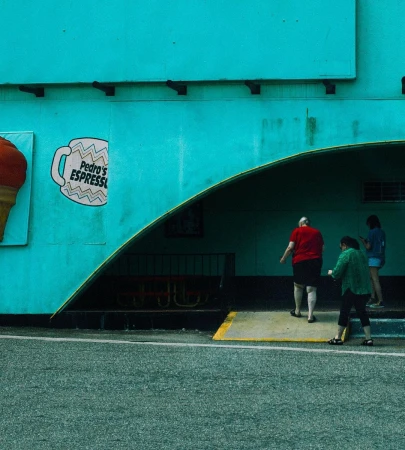 Three people walking near a bright teal building with an arched entrance and a painted coffee mug sign by photographer Andree Ljutica.