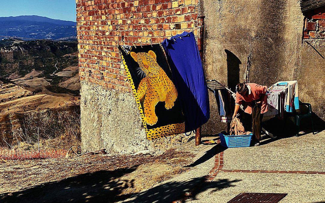 Woman hangs clothes to dry outside next to a brick building with a mountain view, towel with cheetah print, laundry day.
