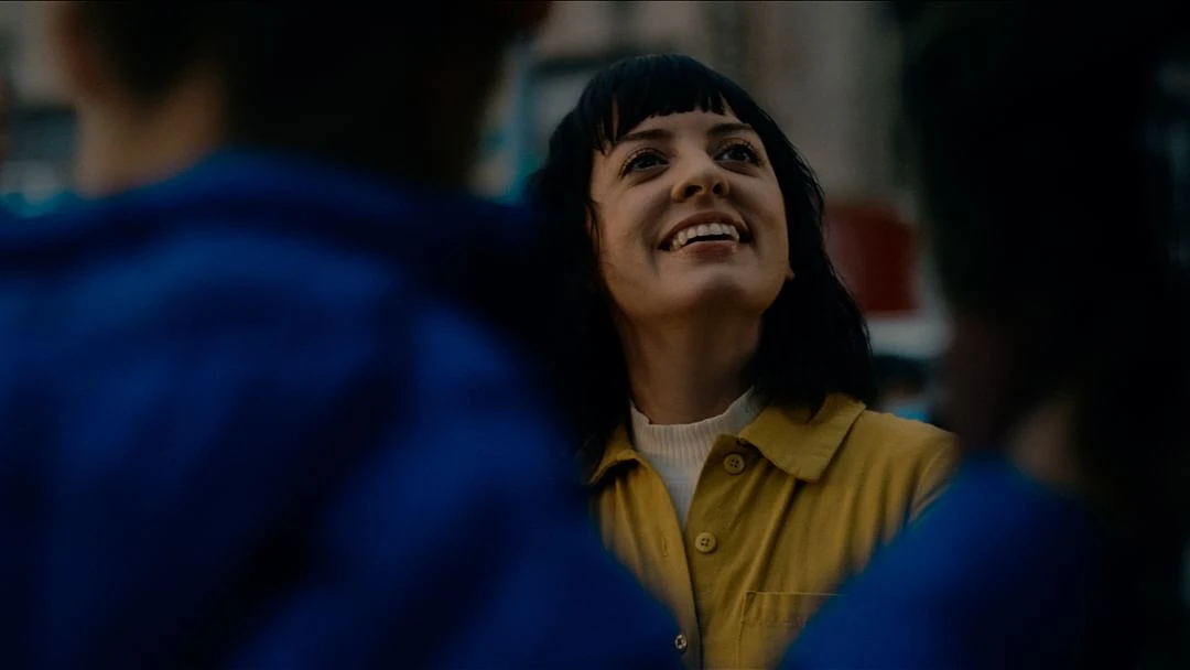 Smiling woman in yellow jacket surrounded by people, captured with a close-up shot, creating a warm and inviting scene.