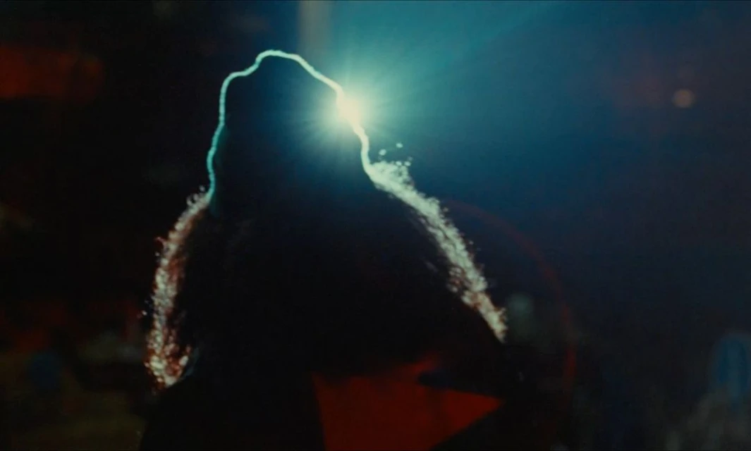 Backlit silhouette of an adult person with curly hair, bathed in dramatic blue light, creating a high-contrast visual.