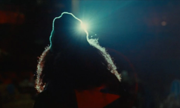 Backlit silhouette of an adult person with curly hair, bathed in dramatic blue light, creating a high-contrast visual.