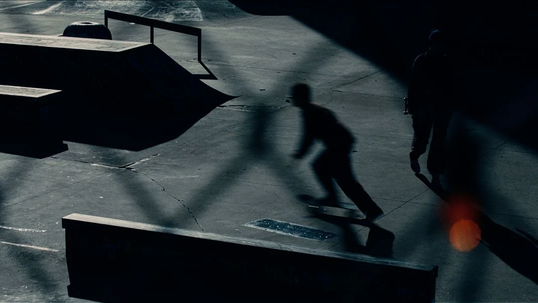 Silhouette of skateboarder in action at a skate park with ramps and railings, under dramatic lighting with long shadows.