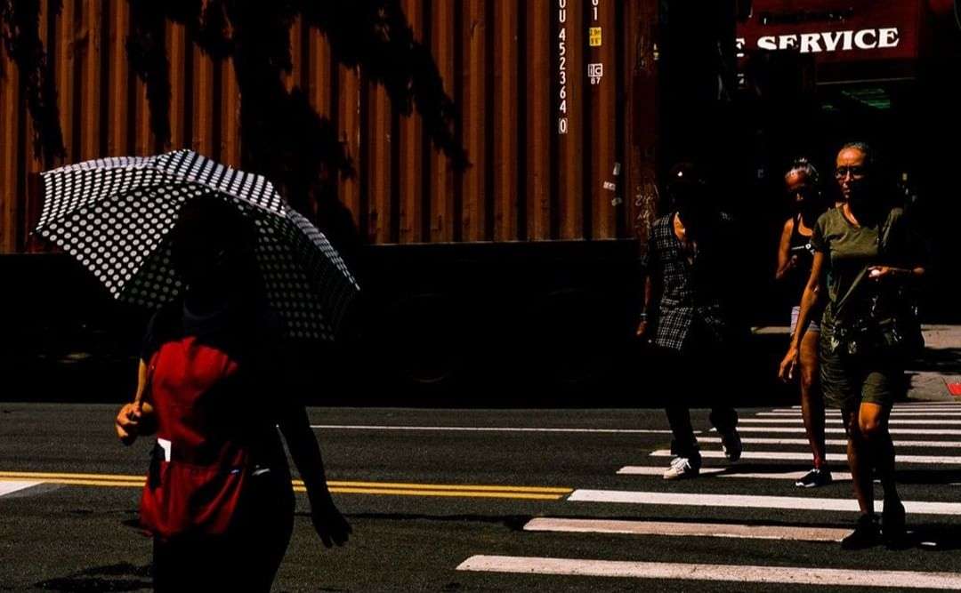 Four people crossing a street with a black and white polka dot umbrella and a dark mood with yellow and white stripes on the crosswalk.