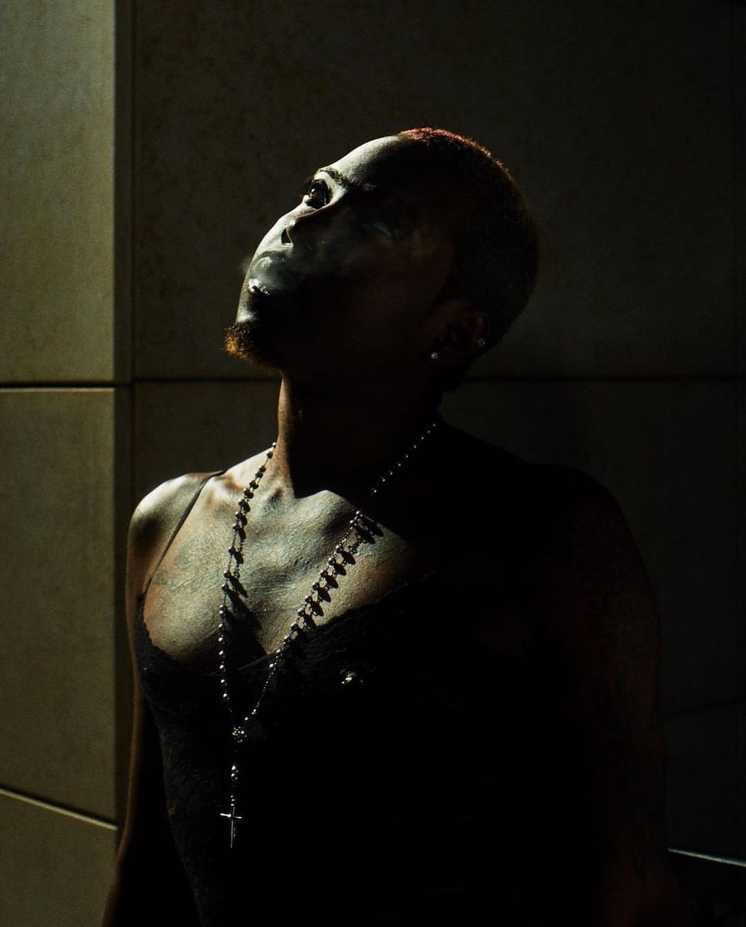 Portrait of a black man with short red hair wearing a black top and silver cross necklace, captured in dramatic low-key lighting.