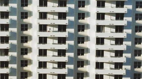 Architectural exterior shot of a white residential building facade with repeating balconies and hard shadows captured by Andree Ljutica
