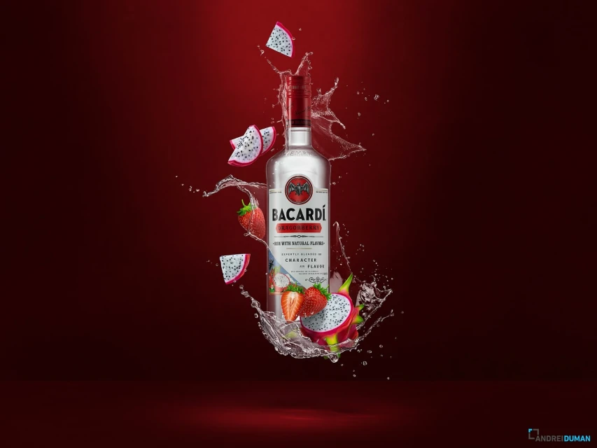 Bacardi bottle surrounded by dragon fruit and strawberries with water splashes set against a vibrant red backdrop in a studio setting.
