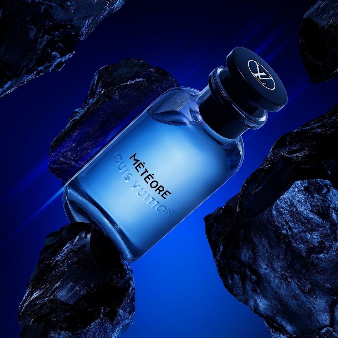 Louis Vuitton Météore fragrance bottle displayed on black rocks against a deep blue backdrop in a beauty and fashion product shot.