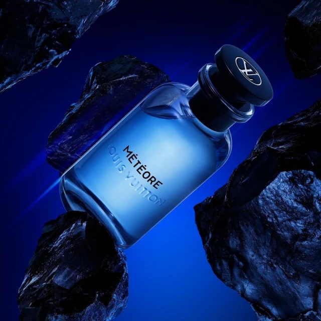 Louis Vuitton Météore fragrance bottle displayed on black rocks against a deep blue backdrop in a beauty and fashion product shot.