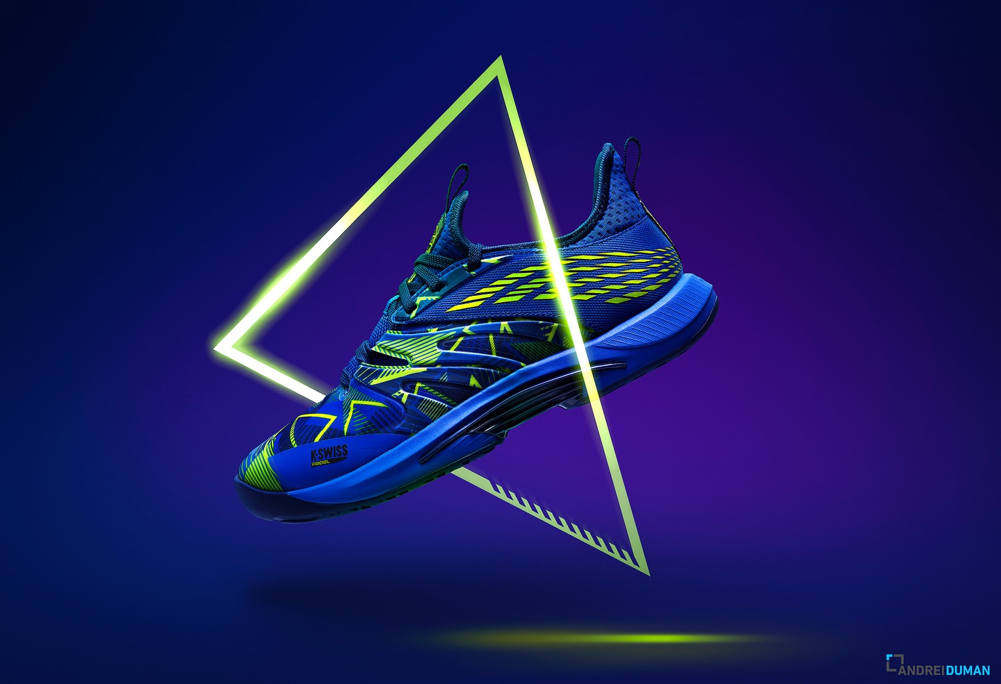 Blue and green K-Swiss tennis shoe levitates against a vibrant blue and purple gradient backdrop with a neon triangle in the background.