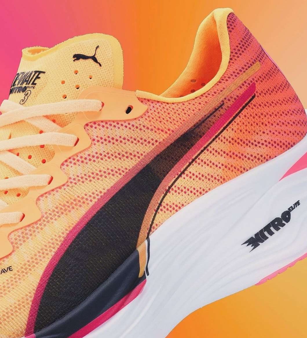 Close-up of a Puma running shoe in shades of orange, yellow, black, and white, showcasing its design and construction details.
