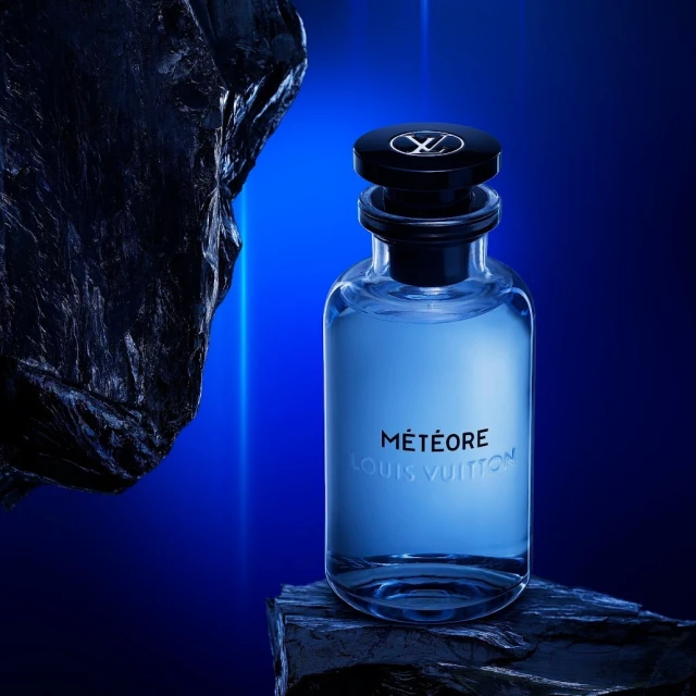 Louis Vuitton Météore perfume bottle displayed on dark rocks against a graduated blue background with a textured black rock fragment.